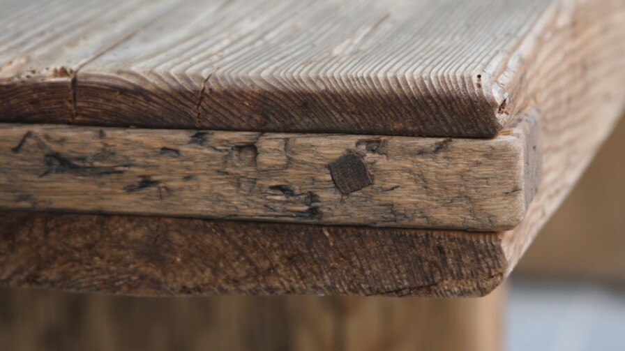 Nahaufnahme einer Altholz-Tischkante mit markanter Maserung, Patina und handwerklichen Verbindungen.