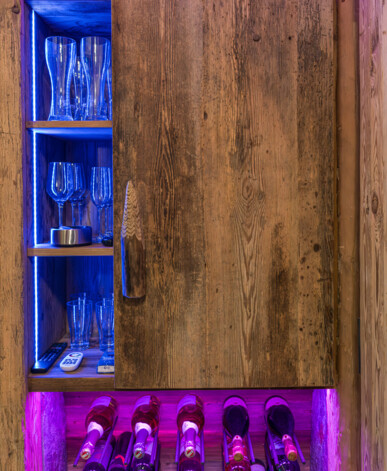 Altholz-Schrank mit beleuchteten Regalen für Gläser und Weinflaschen; stimmungsvolle LED-Beleuchtung in Blau und Violett.