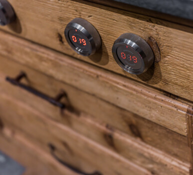 Nahaufnahme einer rustikalen Küchenfront aus Altholz mit Metall-Drehknöpfen und roten LED-Anzeigen.