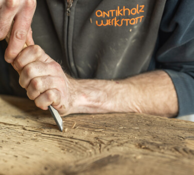 Handwerker bearbeitet Altholz sorgfältig mit Stechbeitel in der Antikholzwerkstatt.
