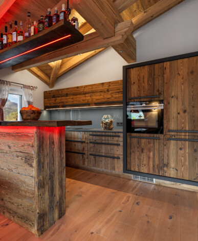 Altholz-Küche mit sichtbaren Dachbalken, Bar mit roter LED, maßgefertigten Fronten und Einbauofen.