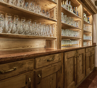 Bar mit Tresen und Schränken aus Altholz, mit offenen Regalen voller Gläser und Flaschen.