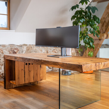 Schreibtisch aus Altholz mit Glasfuß und Curved-Monitor, in einem hellen Loftbüro.