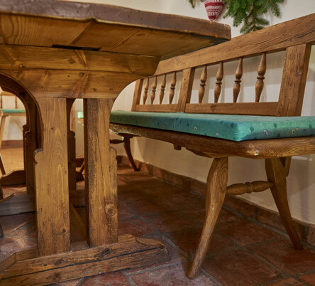 Bank und Tisch aus Altholz mit grünen Sitzpolstern in einer traditionellen Stube.