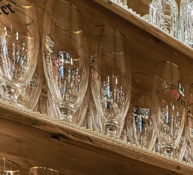 Bar mit Tresen und Schränken aus Altholz, mit offenen Regalen voller Gläser und Flaschen.